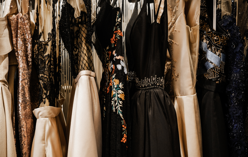 A row of dresses are hanging on a rack in a closet.