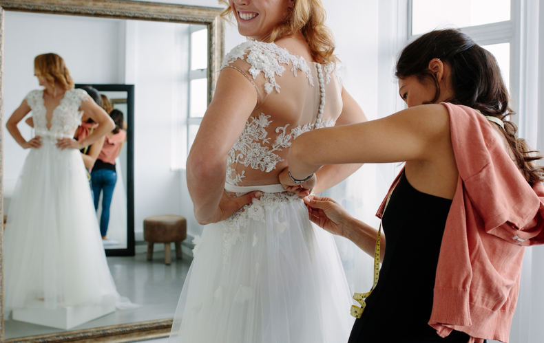 A woman is trying on a wedding dress in front of a mirror.