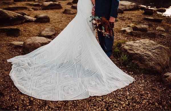 A bride and groom are standing next to each other on a rocky beach.