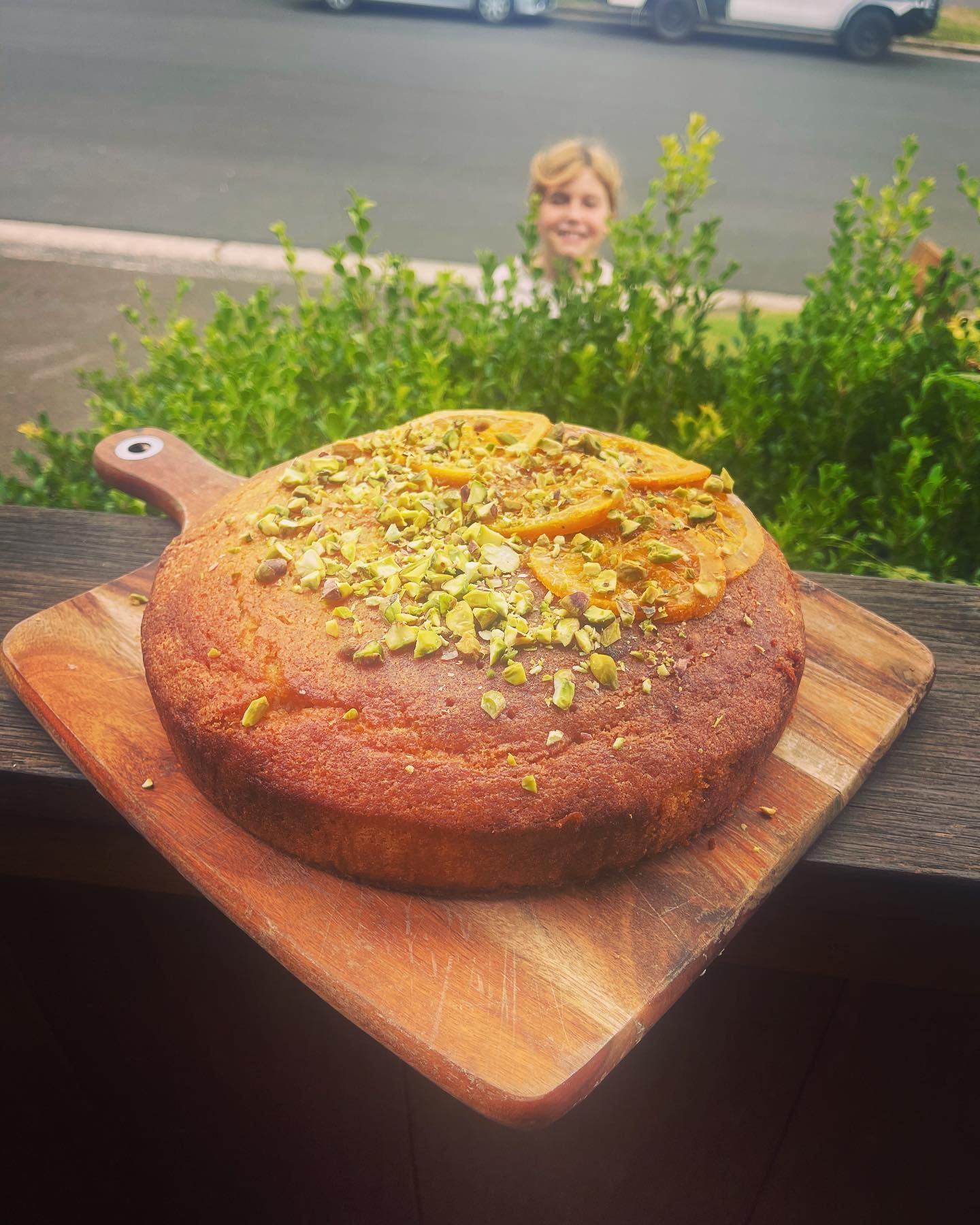 A cake with pistachios on top is sitting on a wooden cutting board.