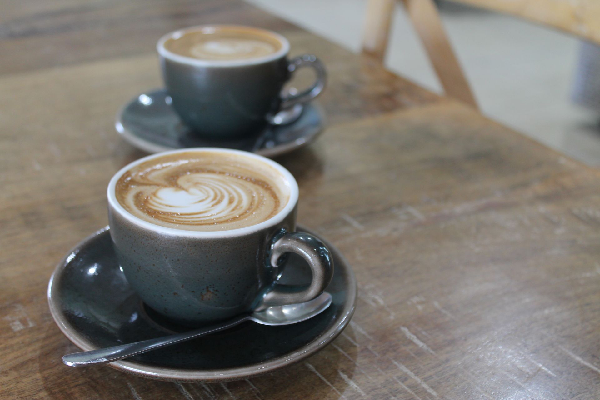 Two cups of cappuccino are sitting on a wooden table.