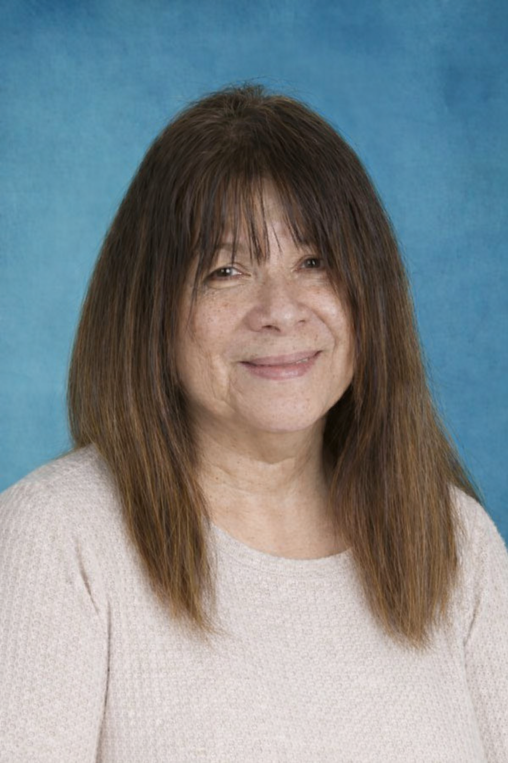 Woman with dark hair and bangs wearing a pink shirt, smiling at the camera.