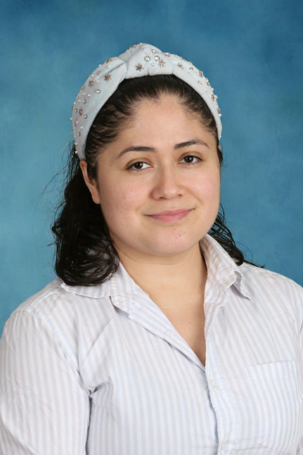 Woman with long dark hair, wearing a white blouse, smiles in front of a blue background.