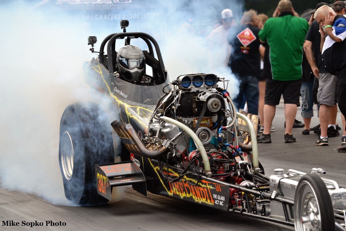 A man is driving a dragster on a race track while people watch.