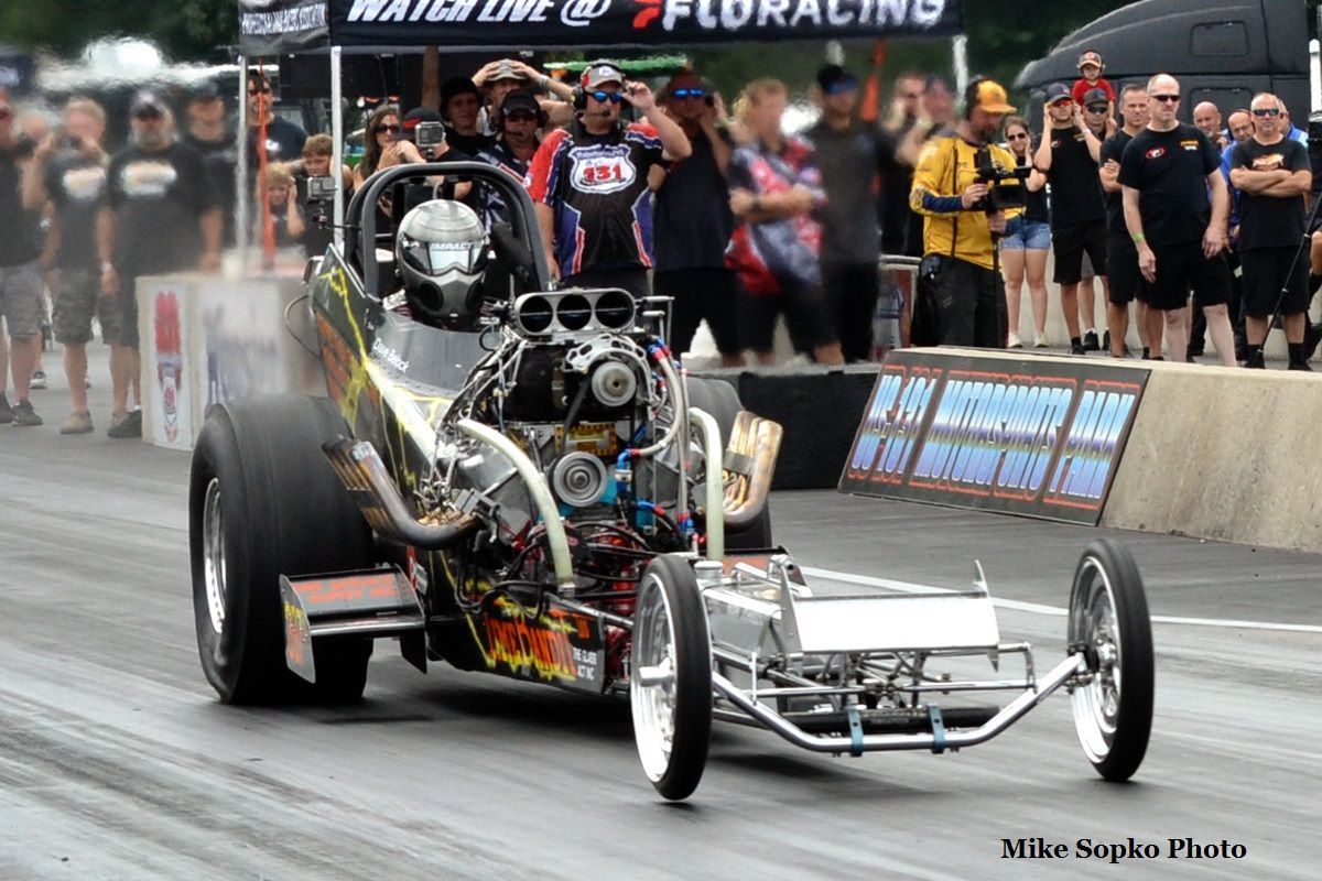 A dragster is driving down a race track with a crowd watching.