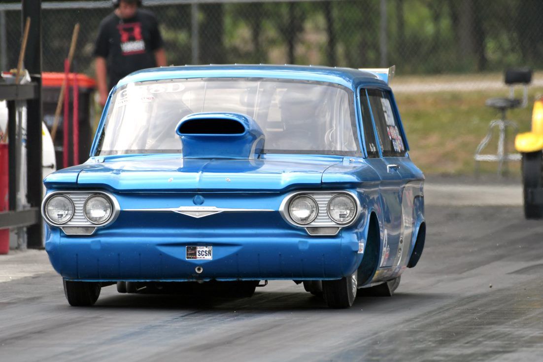 A blue car with a hood scoop is driving down a race track