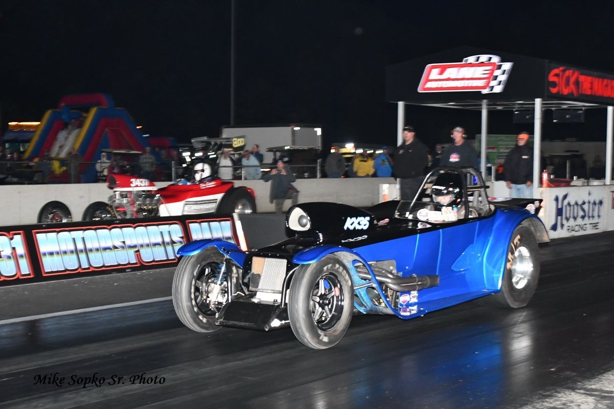 A blue car is driving down a race track next to a sign that says vespert