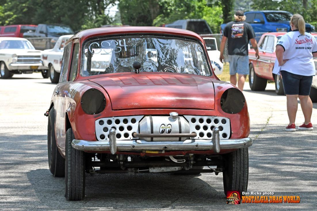 A red car is parked in a parking lot with people standing around it.