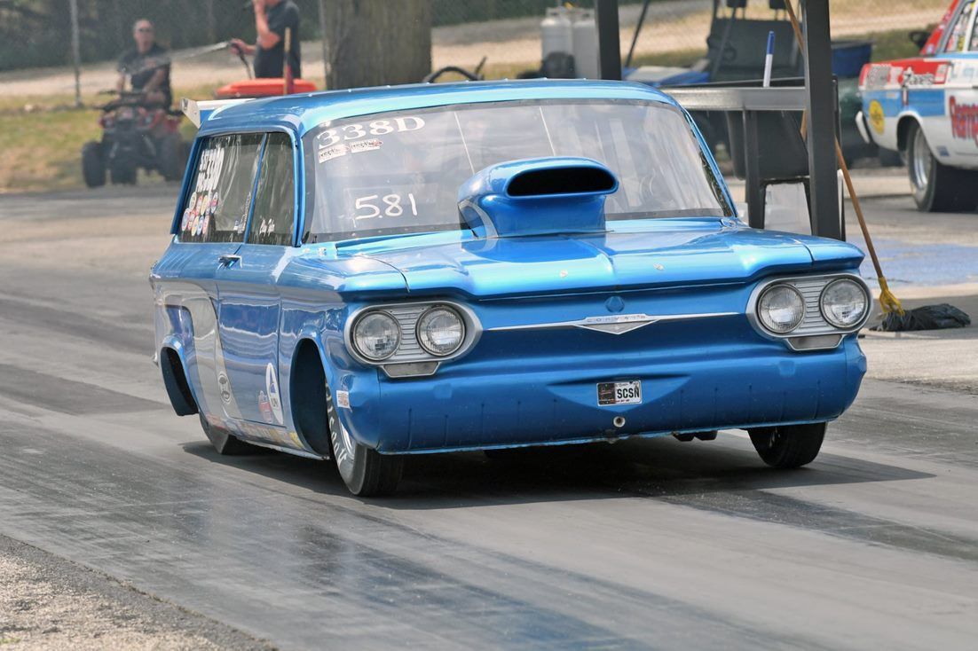 A blue car with a hood scoop is driving down a road.