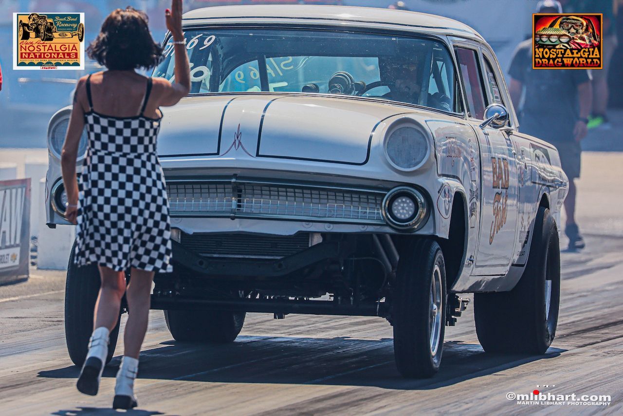A woman in a checkered dress is waving at a white car on a race track.