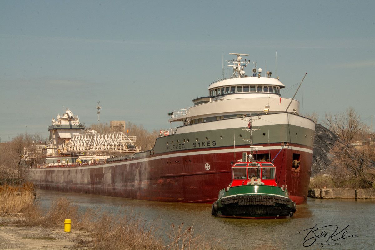 A large red and green ship is being towed by a tugboat.
