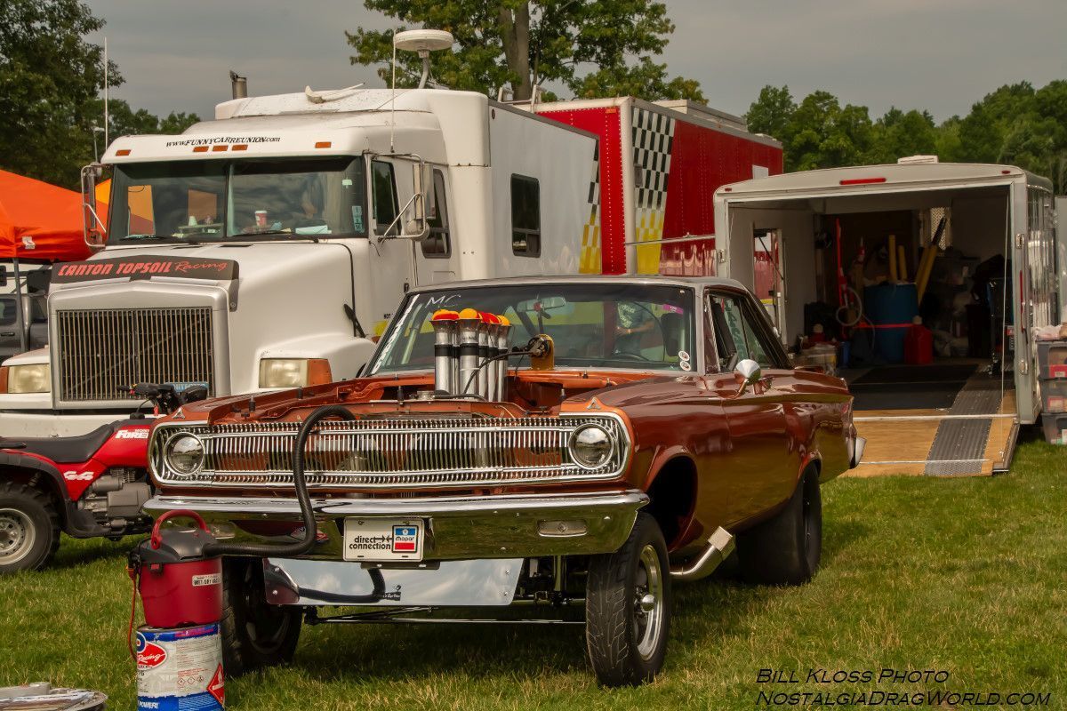 A car is parked in a grassy field next to a truck.