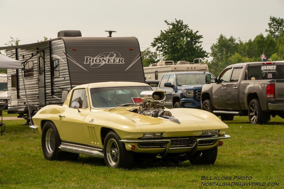 A yellow corvette is parked in a grassy field next to a trailer.