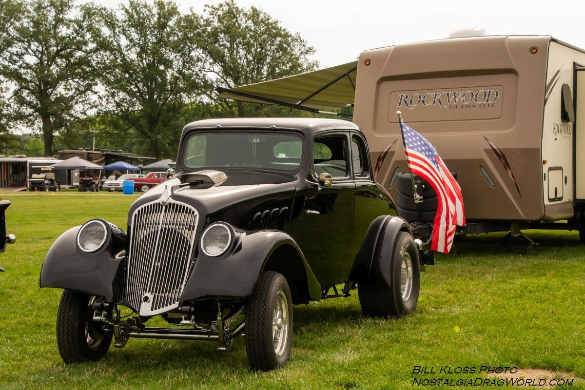 A black car is parked in a grassy field next to a trailer.