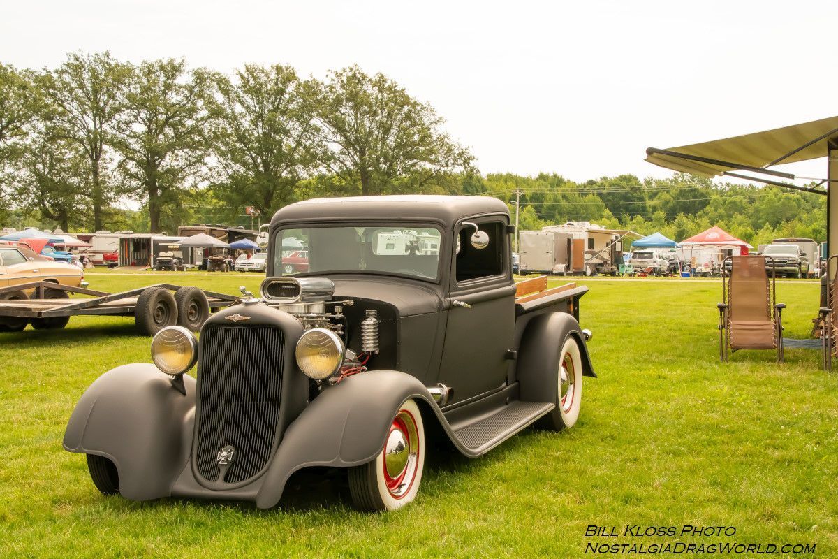 An old black truck is parked in a grassy field.