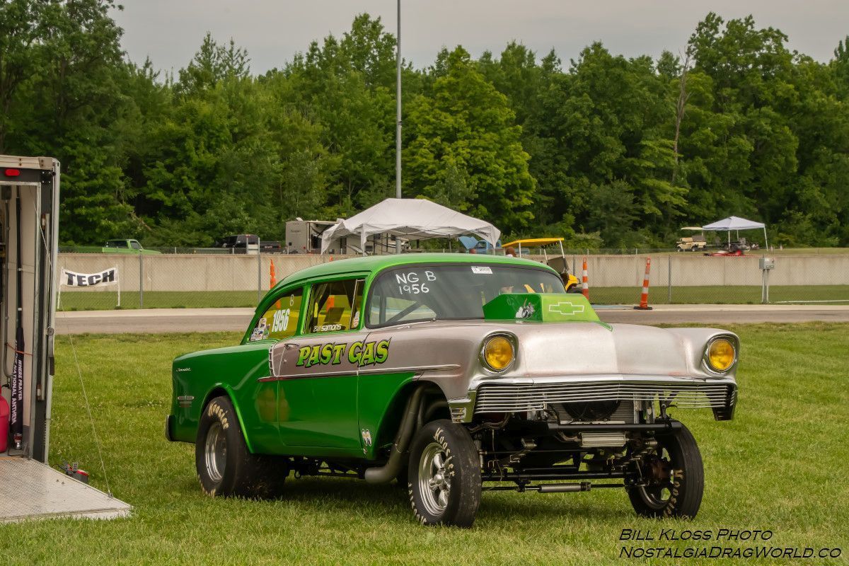 A green and silver car is parked in a grassy field next to a trailer.