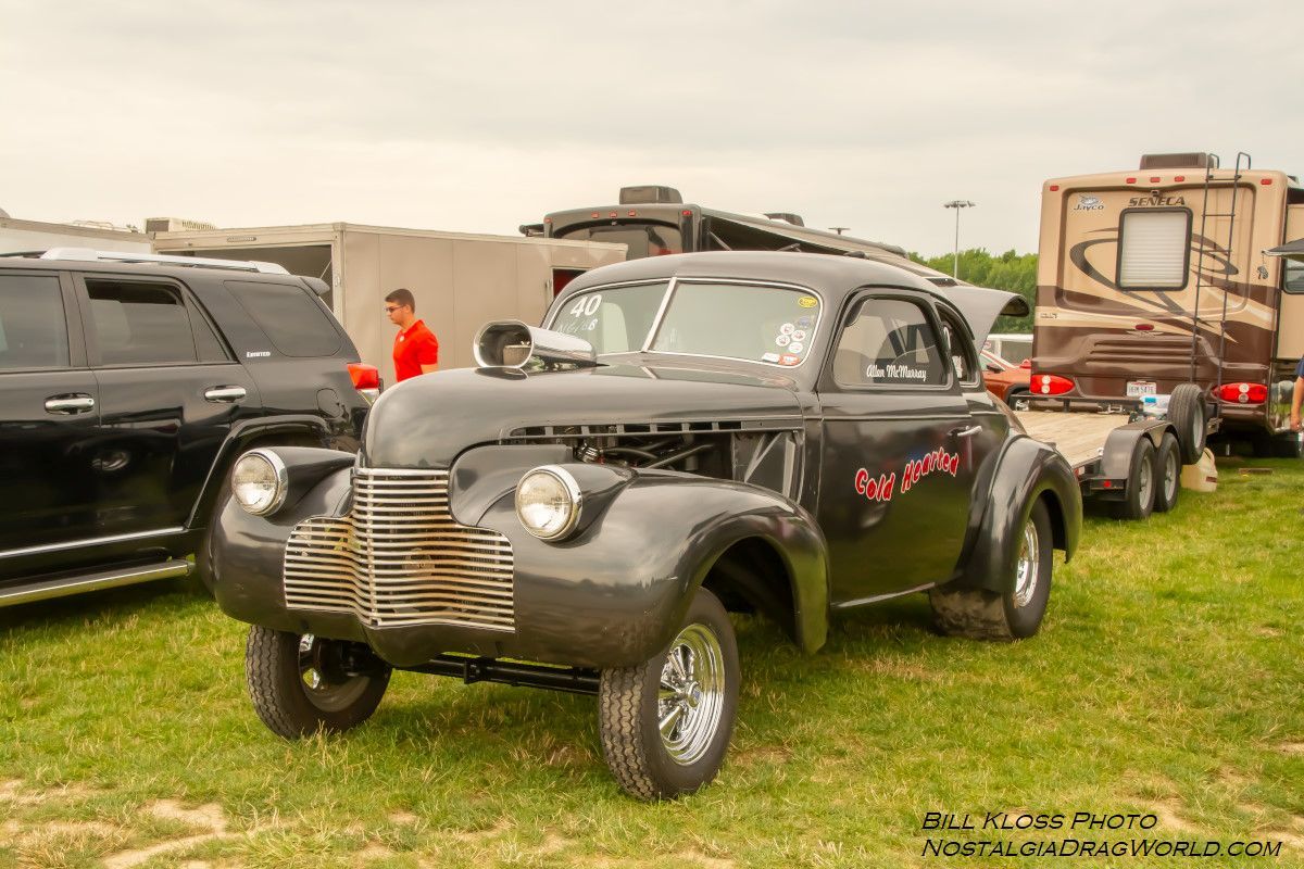 A black car is parked in a grassy field next to a trailer.