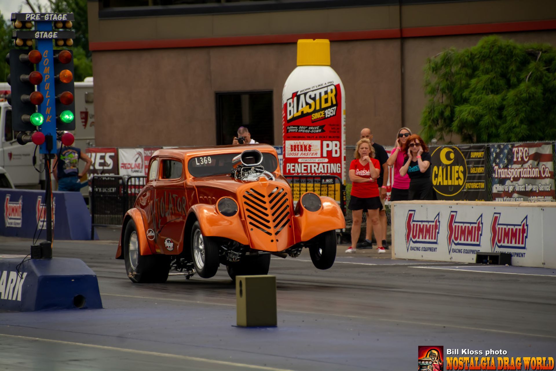 An orange car is driving down a race track next to a bottle of buster