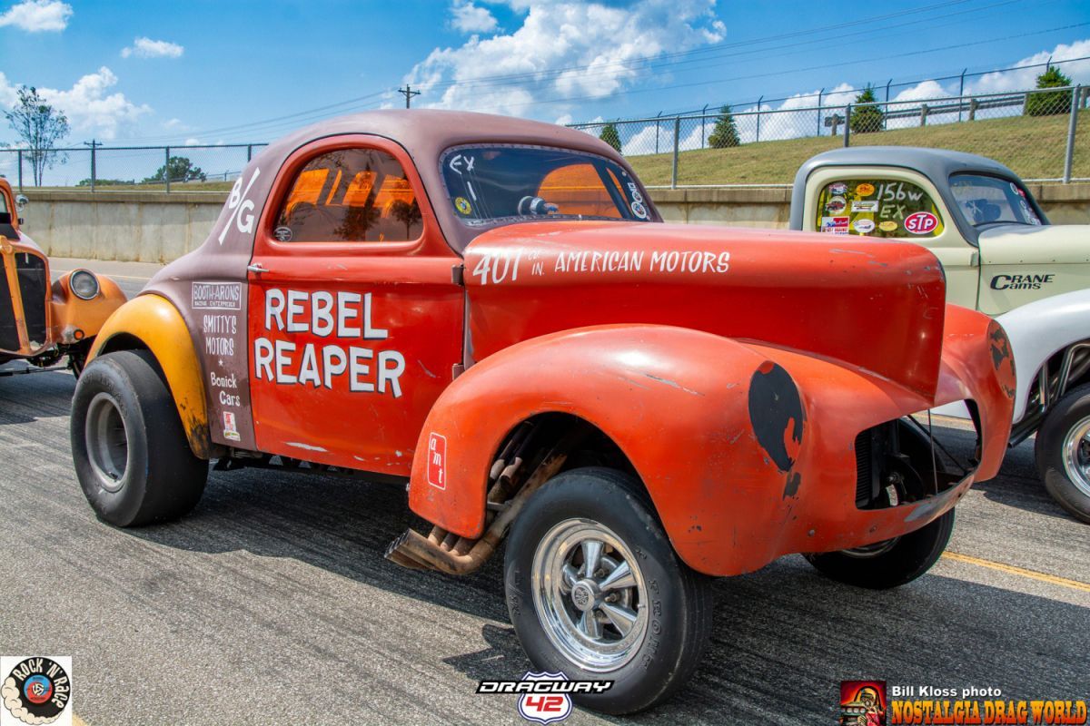 A red car with rebel reaper written on it is parked on the side of the road.