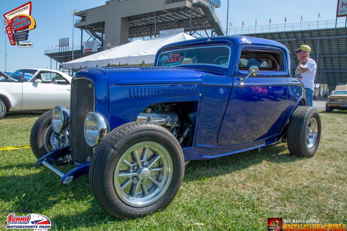 A blue car is parked in the grass at a car show.