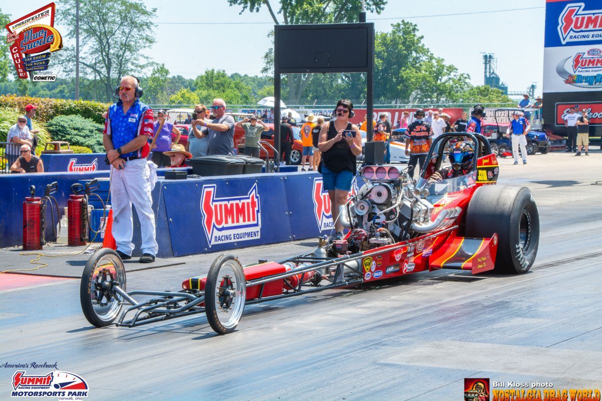A red and black dragster is driving down a race track.