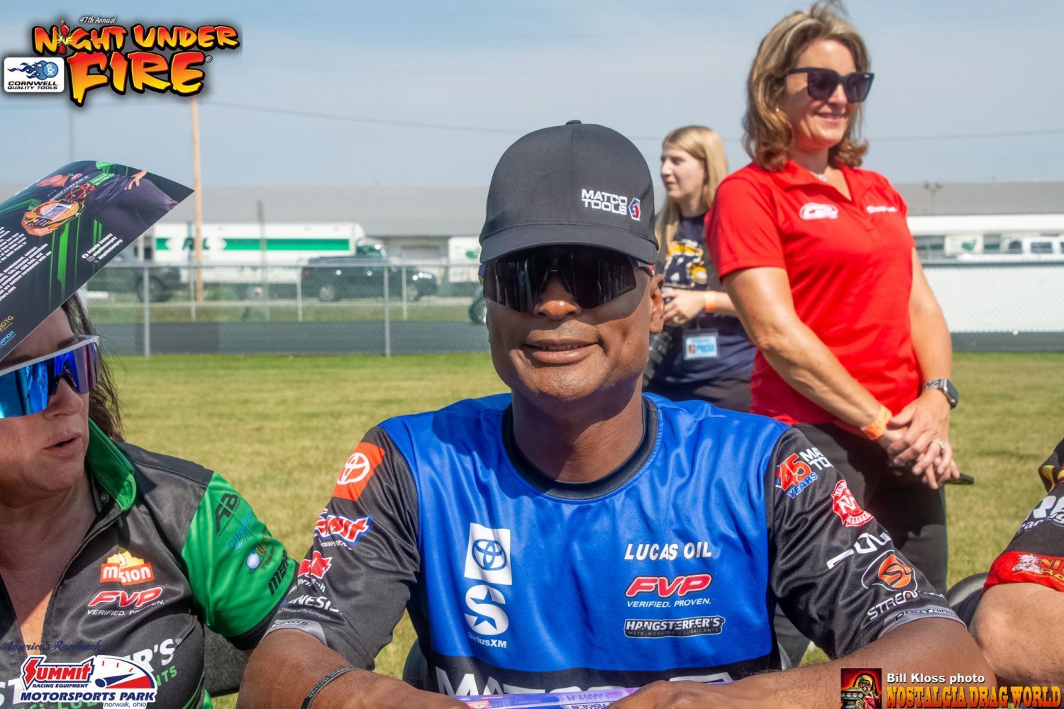 A man wearing a hat and sunglasses is sitting in front of a group of people.