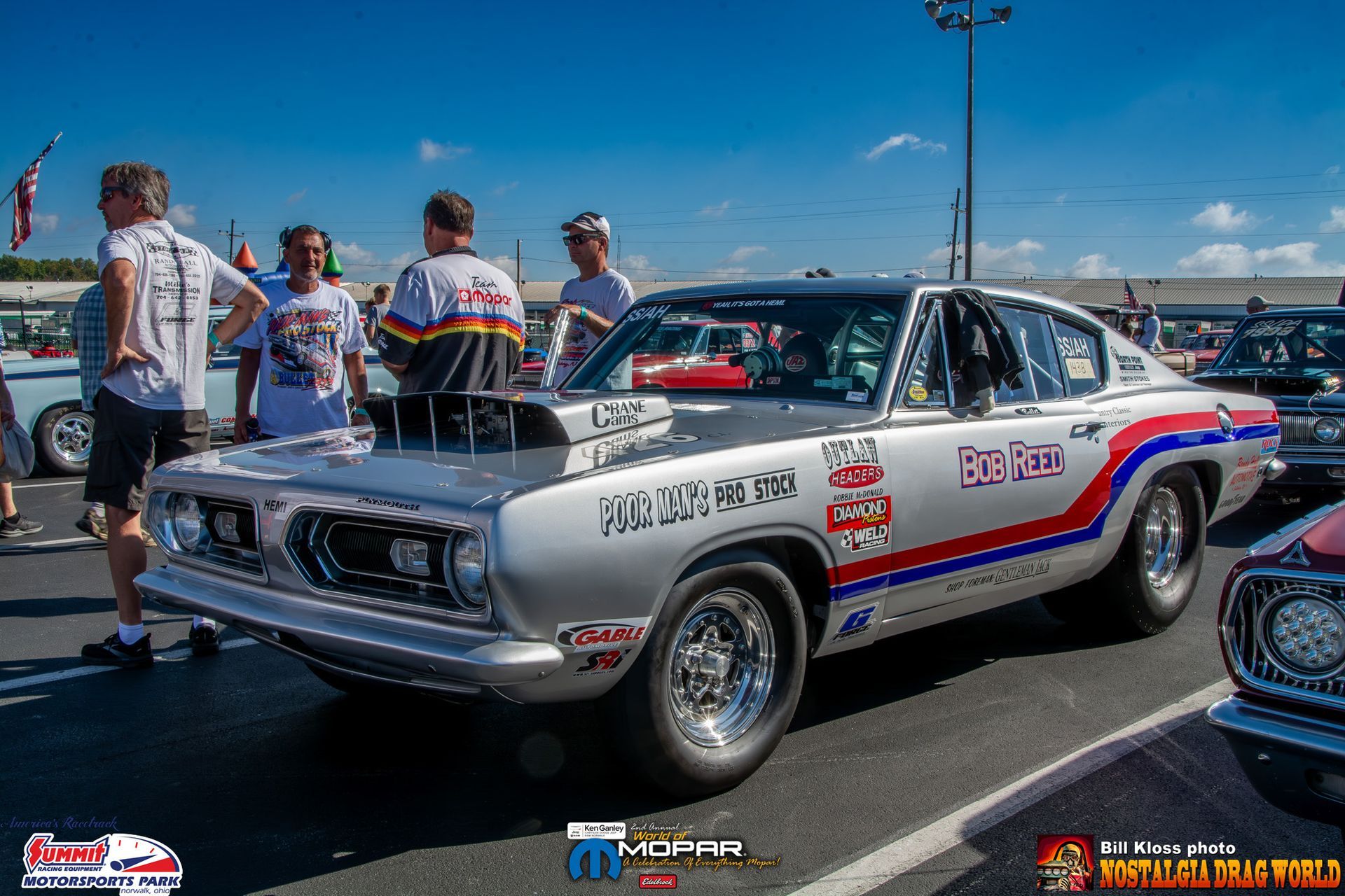 A group of people are standing around a race car parked in a parking lot.
