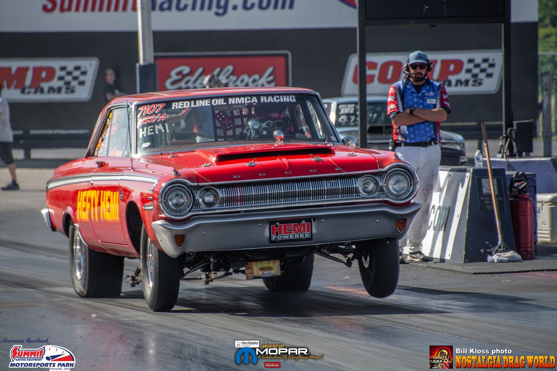 A man is standing next to a red car on a race track.