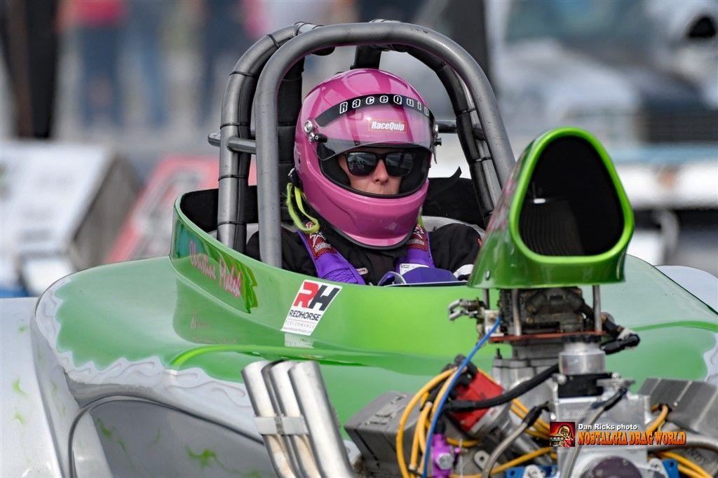 A woman in a pink helmet is sitting in a green race car.