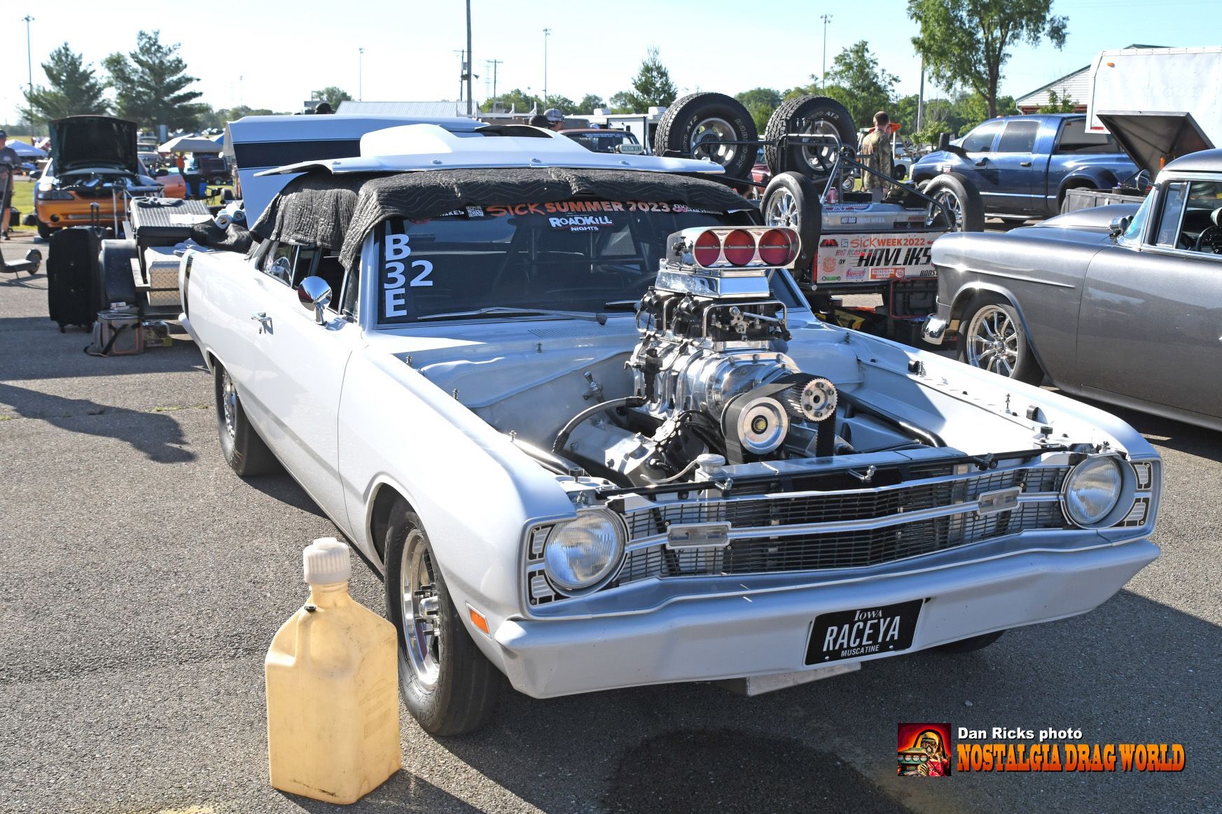 A white car with a big engine is parked in a parking lot