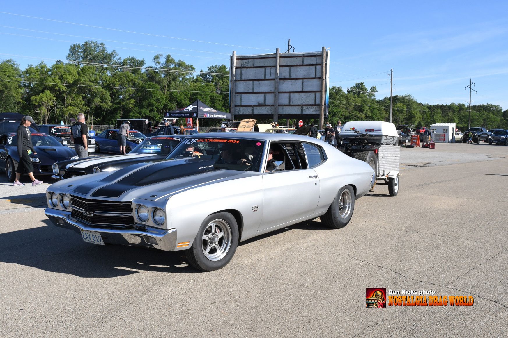 A silver car is parked in a parking lot next to a trailer.