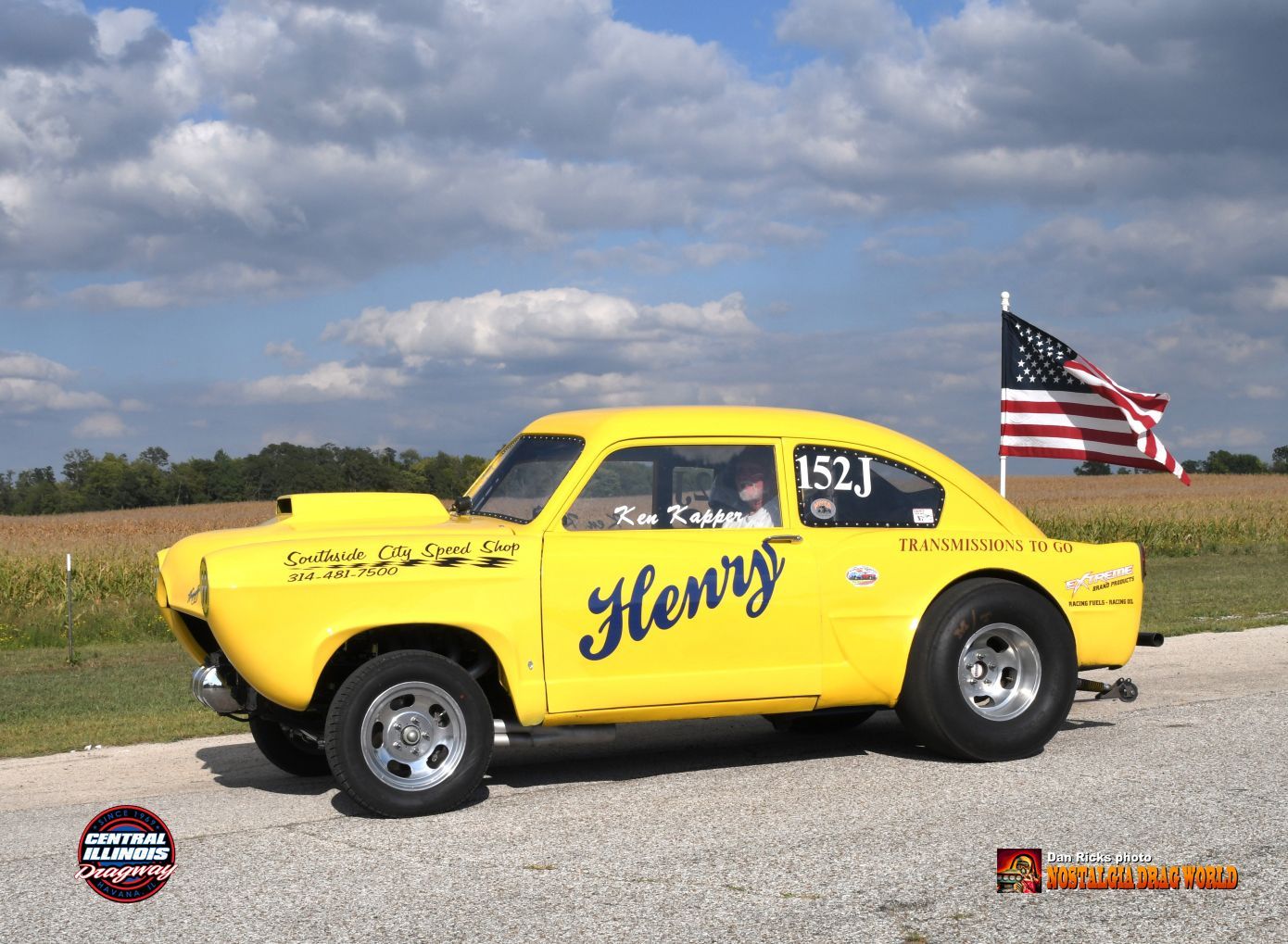 A yellow race car with the name henry on the side is parked on the side of the road.