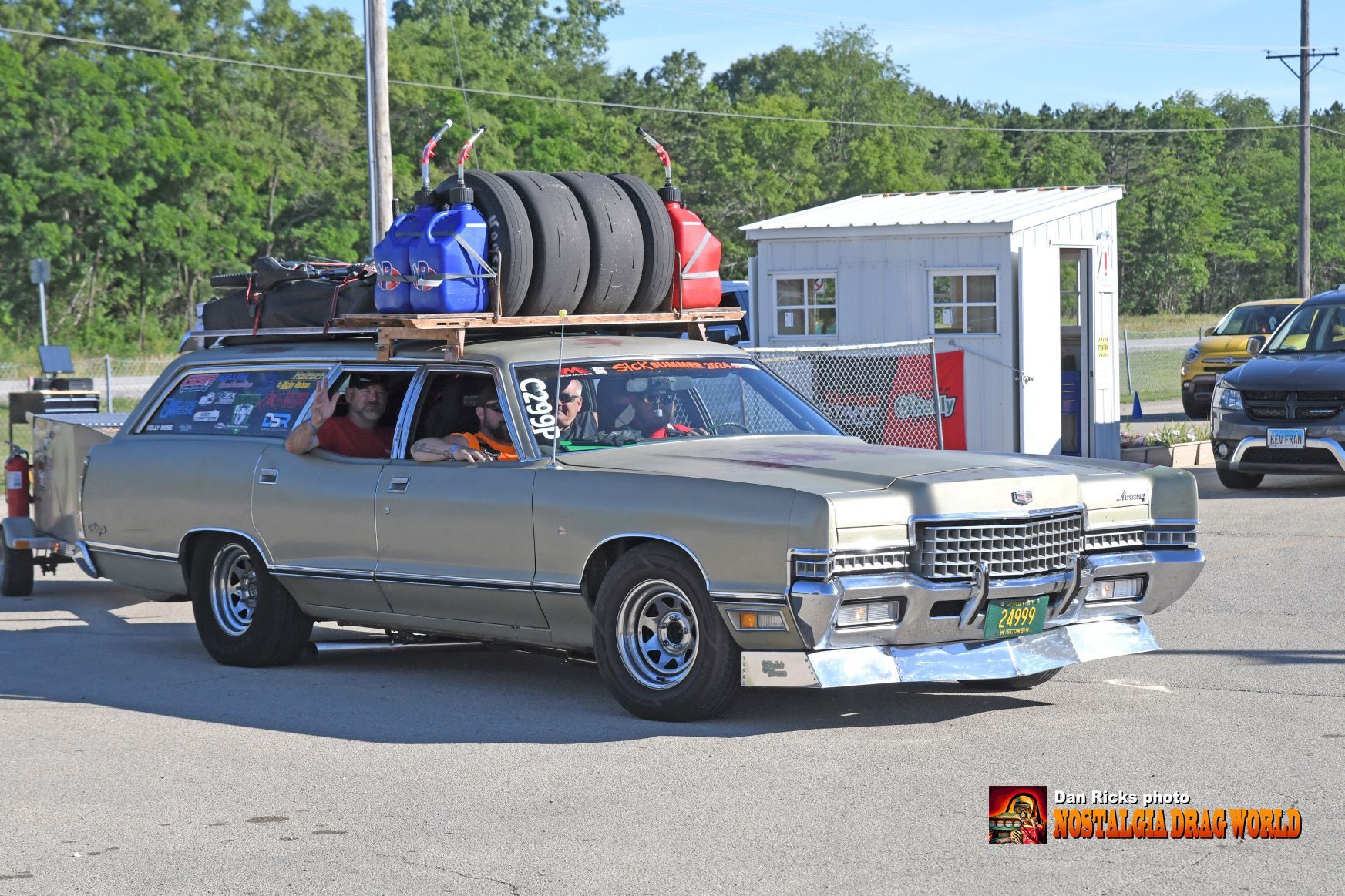A silver car with tires on top of it is parked in a parking lot.