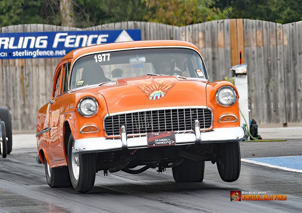 An orange car with the number 1977 on the windshield is driving down a race track.