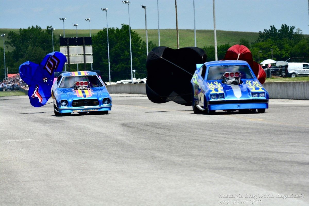 Two blue race cars are racing on a track and one has the number 1 on it