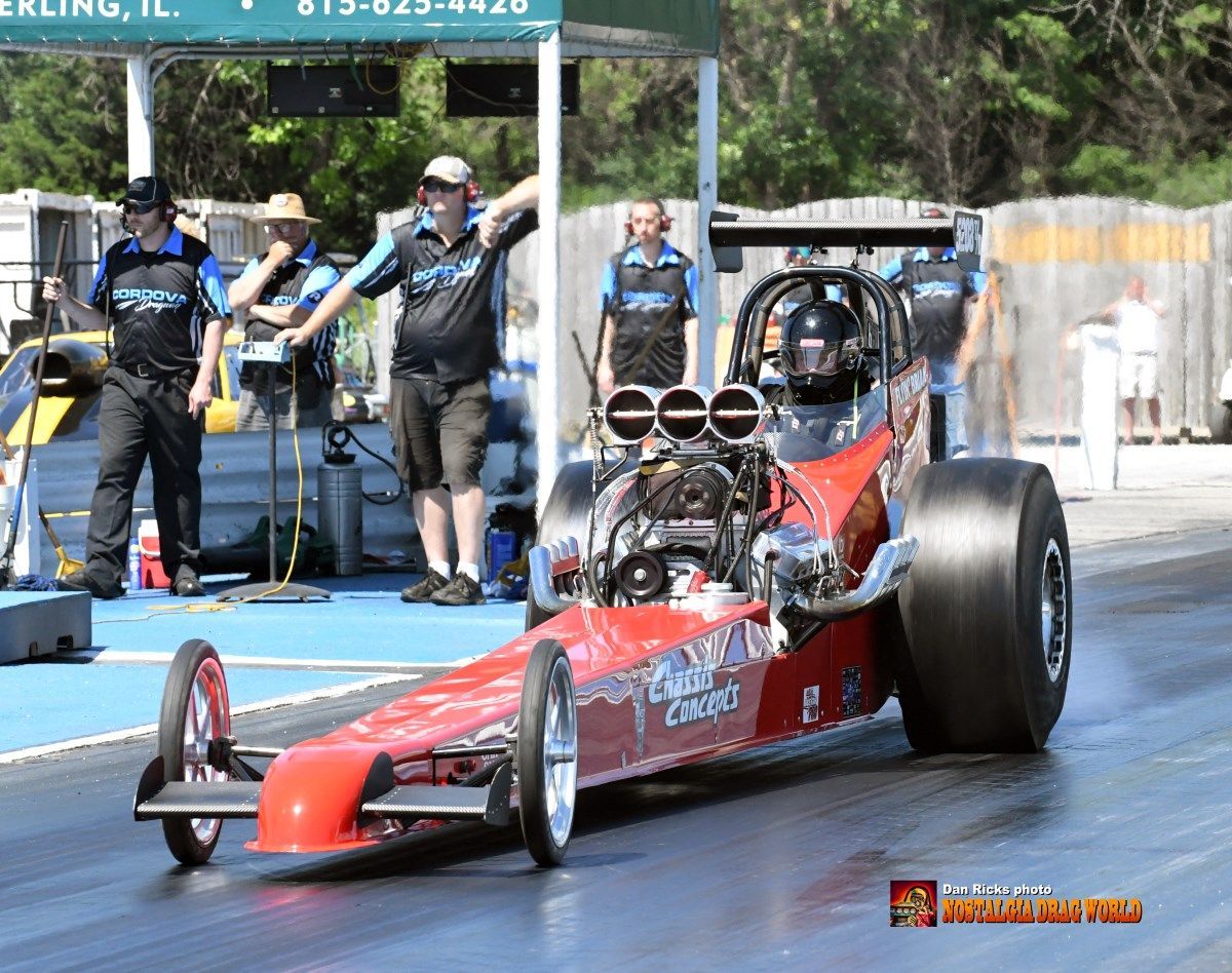 A red race car is on a track with people standing around it.
