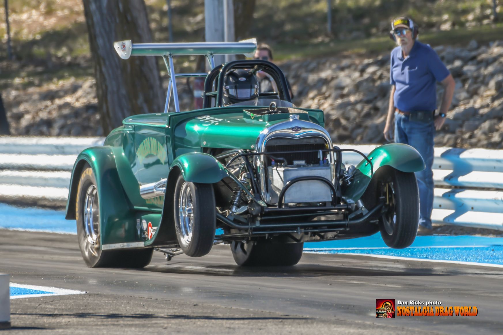 A man is standing next to a green car on a race track.