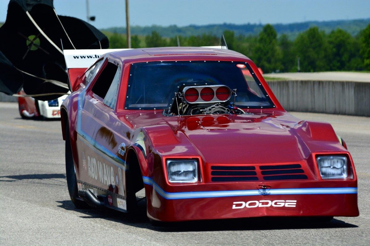 A red dodge race car is driving down a road