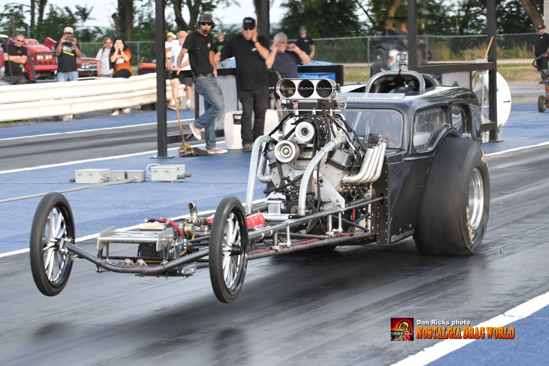 A dragster is driving down a race track with people watching.