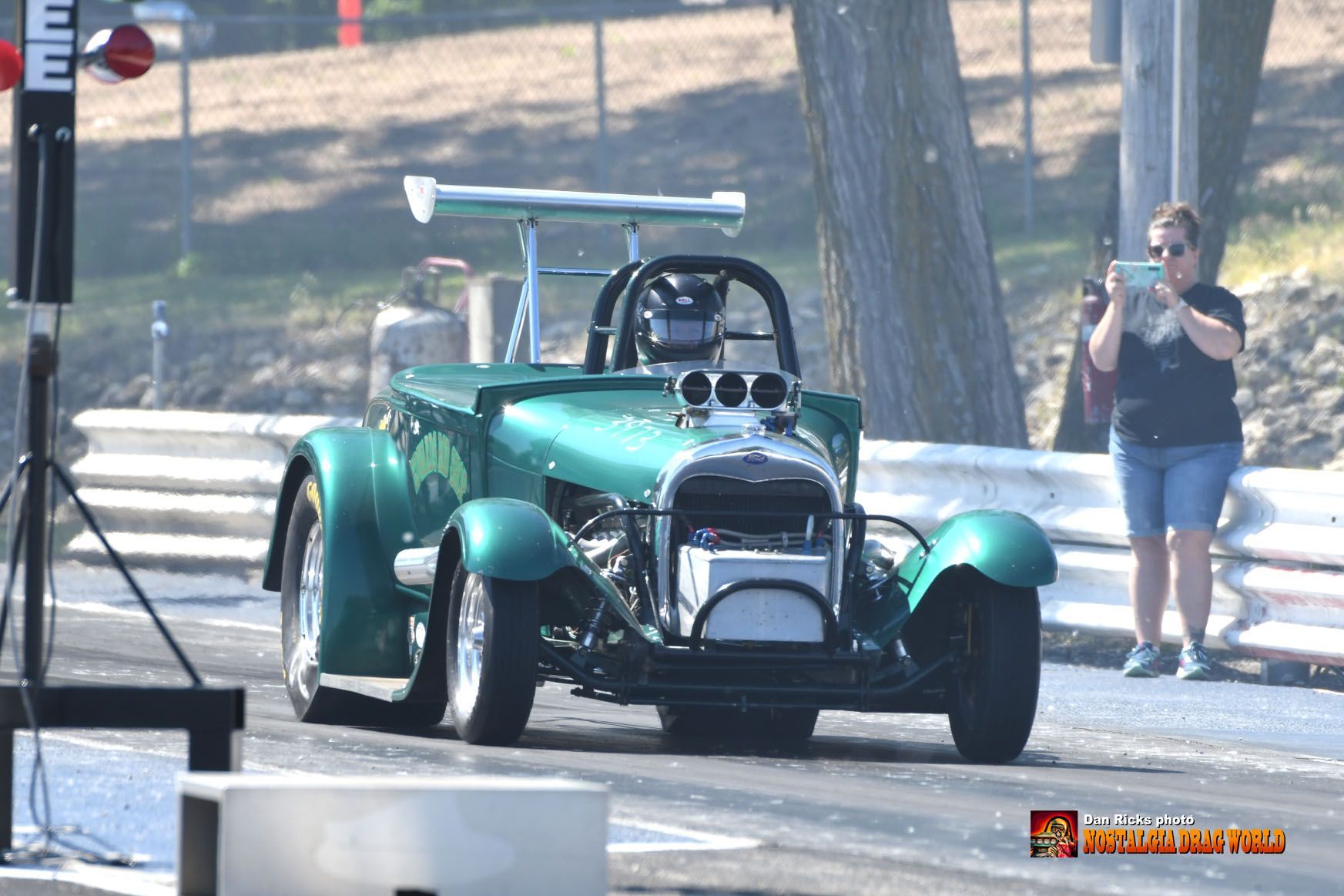 A woman is taking a picture of a green car on a race track.