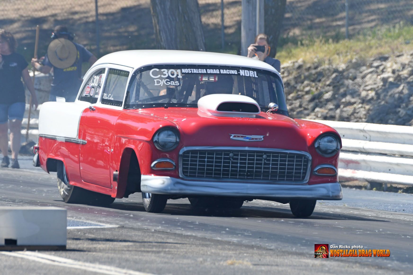 A red and white car is driving down a road.