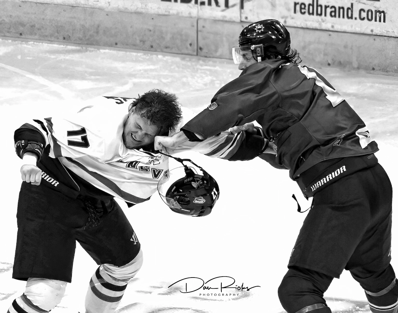 Two hockey players are fighting on the ice and one has the number 12 on his jersey