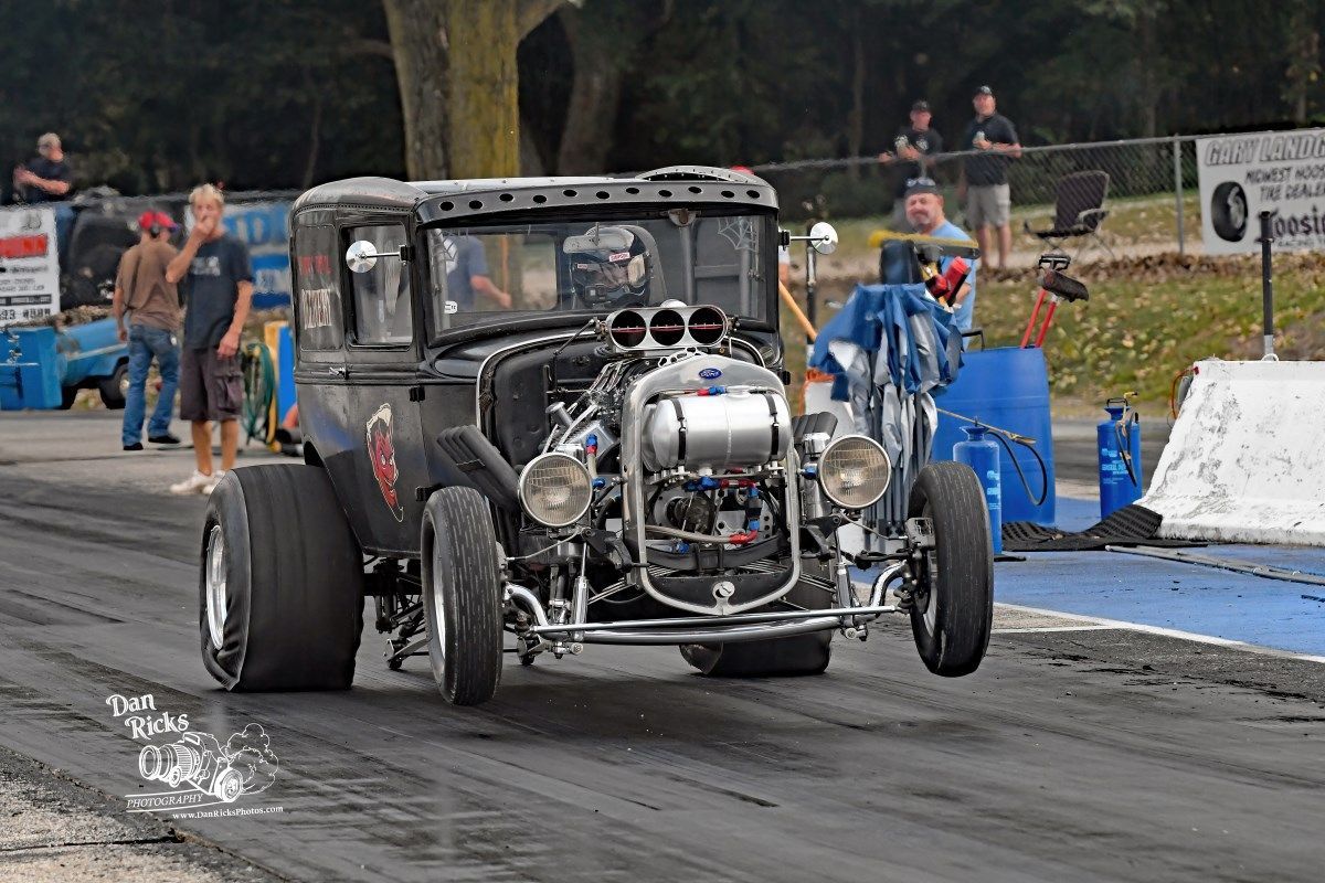 A black hot rod is driving down a race track.
