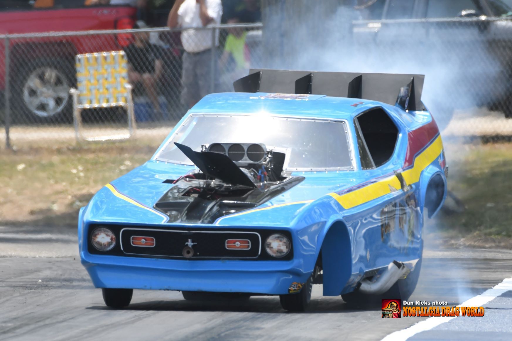 A blue race car is driving down a track with smoke coming out of the hood.