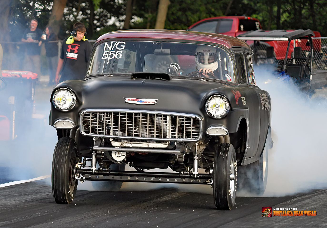 A black car with smoke coming out of it is driving down a race track.
