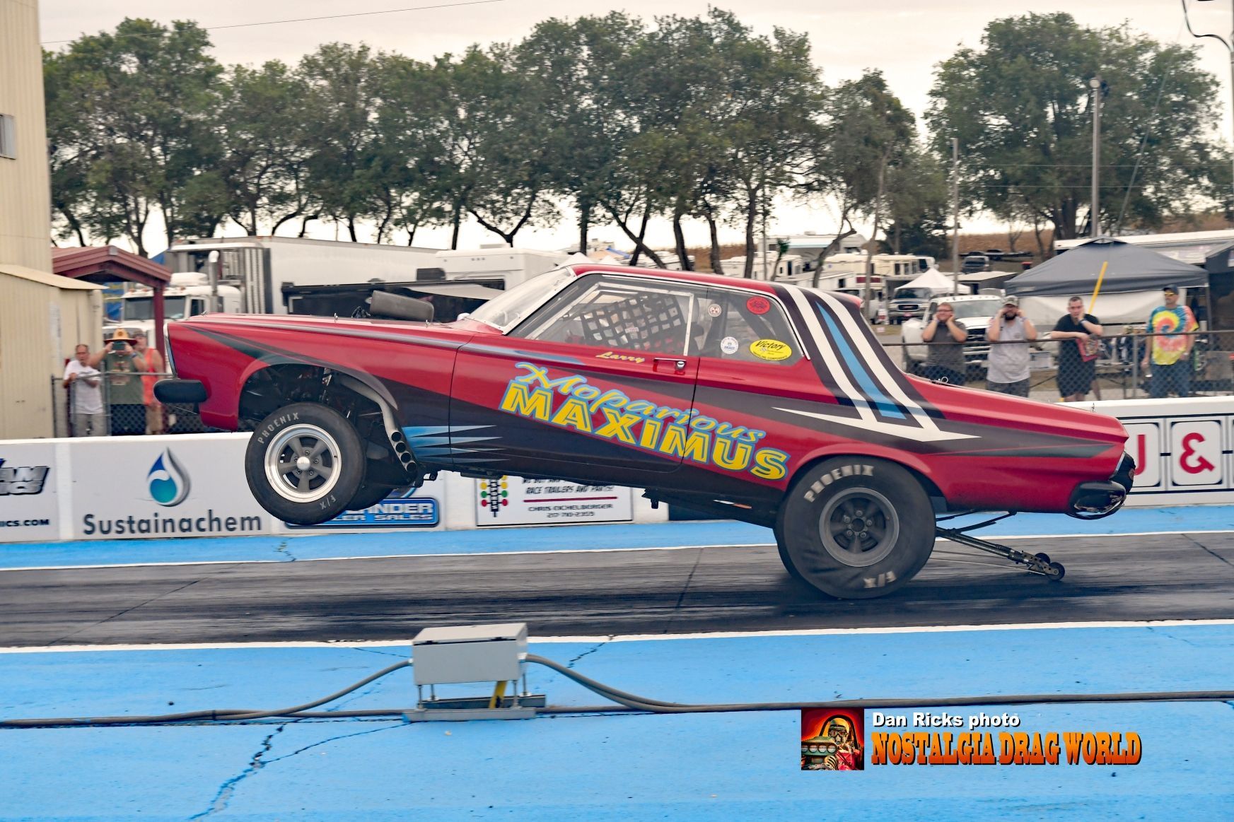 A red car with the word maximus on the side is on a race track.