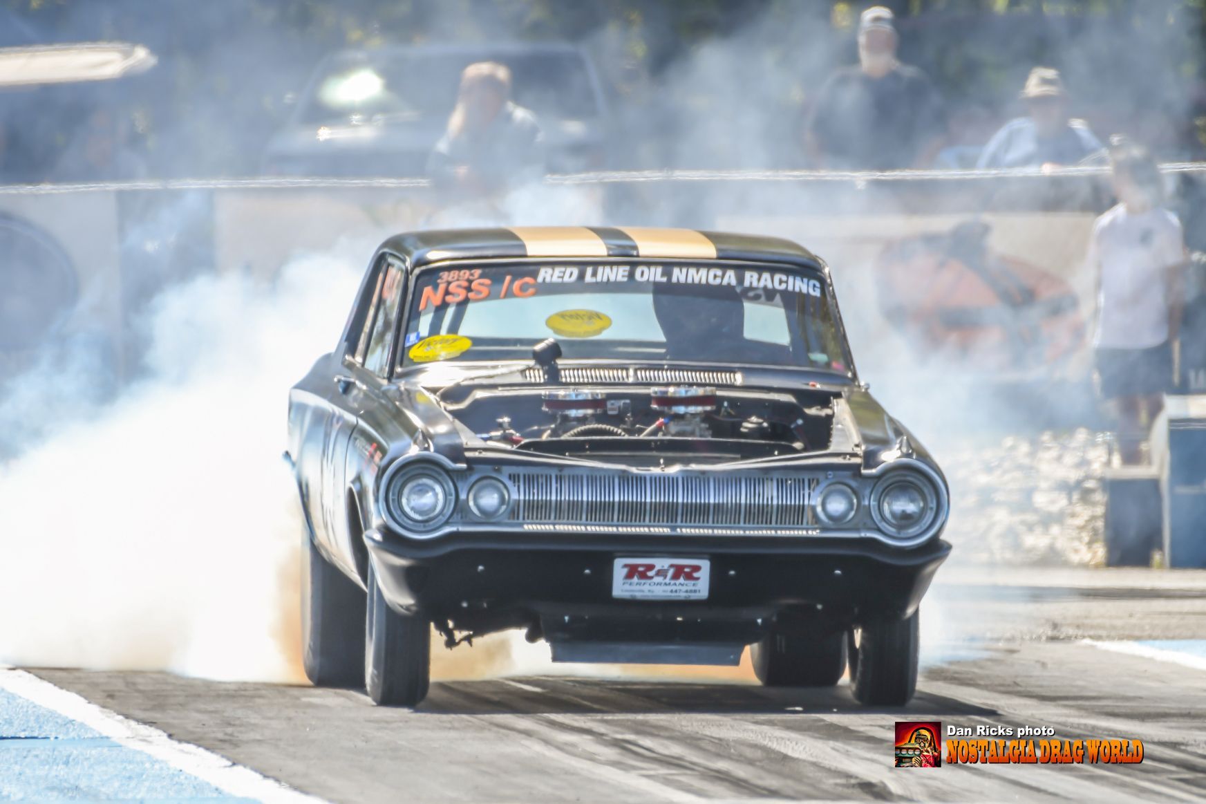 A black and yellow race car is doing a burnout on a track.