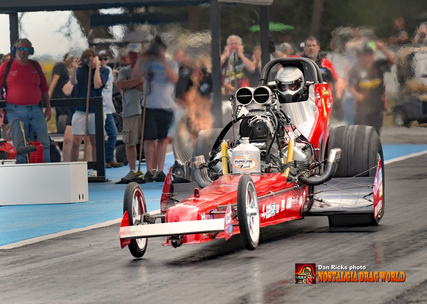 A red dragster is driving down a race track.