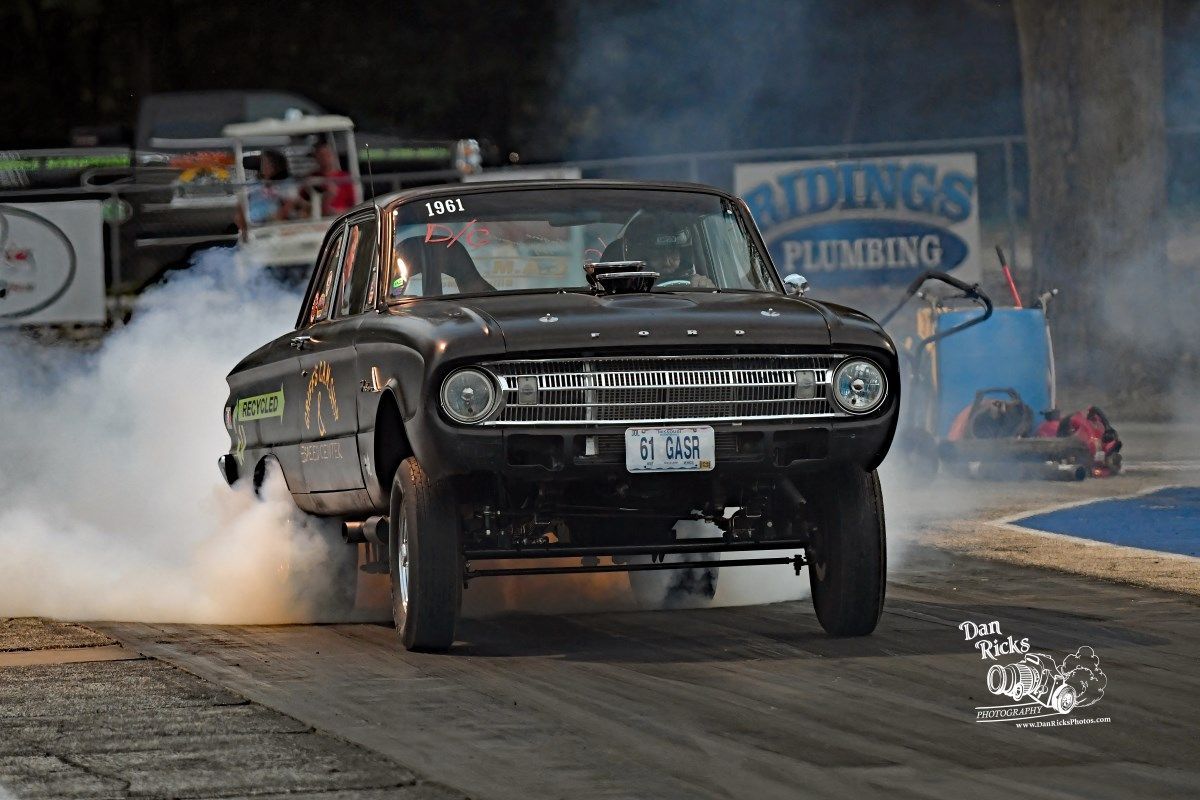 A black car is doing a burnout on a race track.