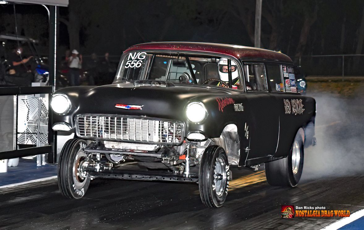 A black car is driving down a race track at night
